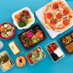A top-down shot of many different types of take-out food in containers on a turquoise backdrop