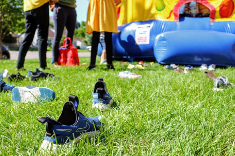 Shoes lying in green grass and kids standing outside a colorful bouncy house