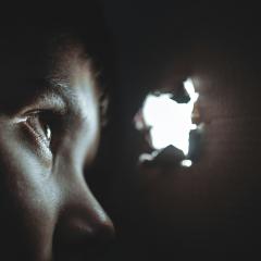 A child’s face peers at light coming through a hole into a dark space.