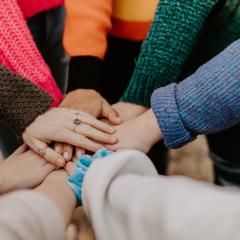 Hands coming together stacked on top of each other, with colorful sleeves and jewelry