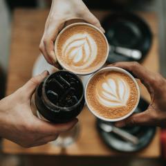 three beverages being cheers'ed together, two are lattes and one is a cold drink with ice.