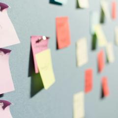 Out of focus post it notes on a light green wall. One close up post it note reads impact-ful. 