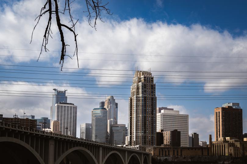 The Minneapolis skyline with the Stone Arch Bridge in the foreground and blue sky and white clouds in the background.