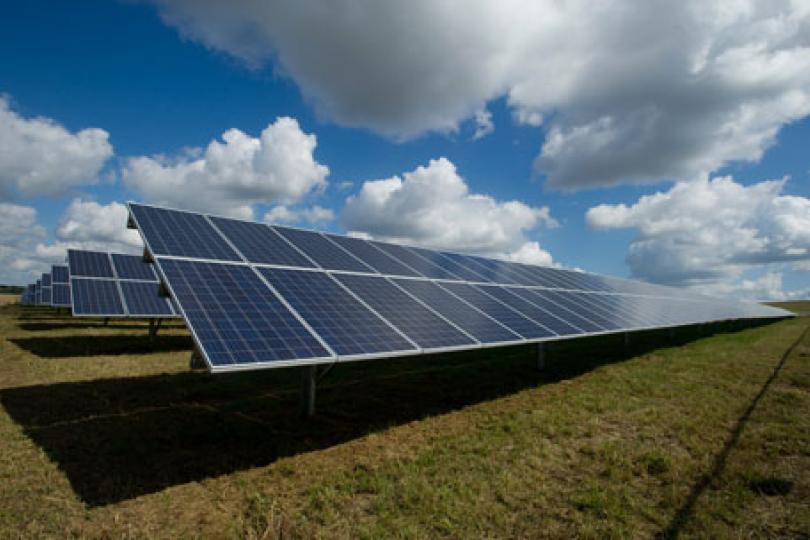 A field of solar panels against a background of blue sky and clouds