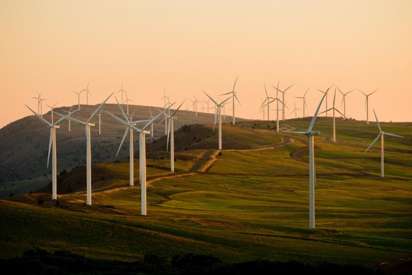 Windmills on a grassy hill lit by a sunset from a distance