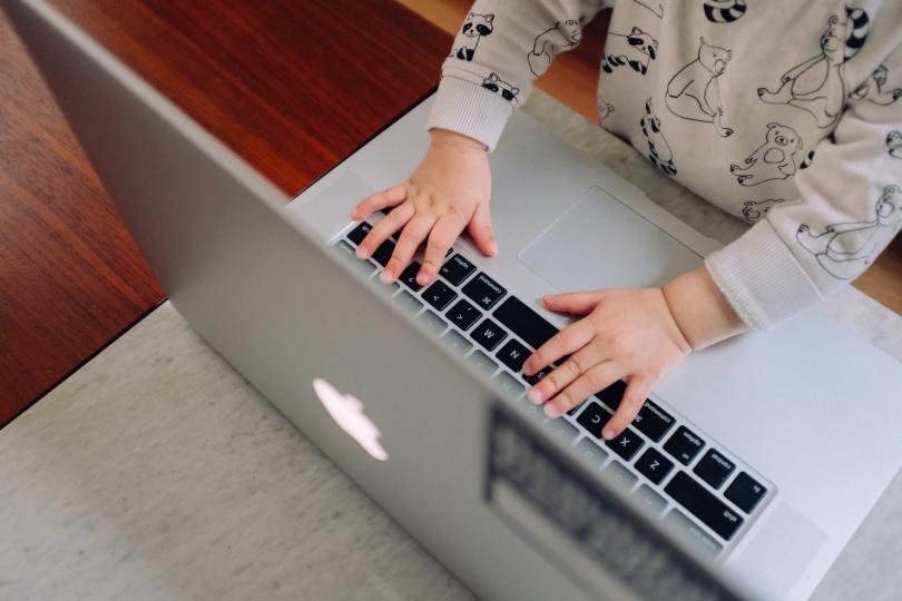 A toddler's hands appear to type on a laptop keyboard