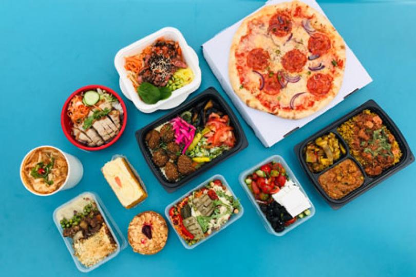 A top-down shot of many different types of take-out food in containers on a turquoise backdrop