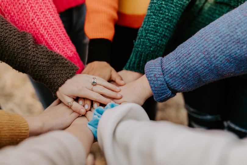 Hands coming together stacked on top of each other, with colorful sleeves and jewelry