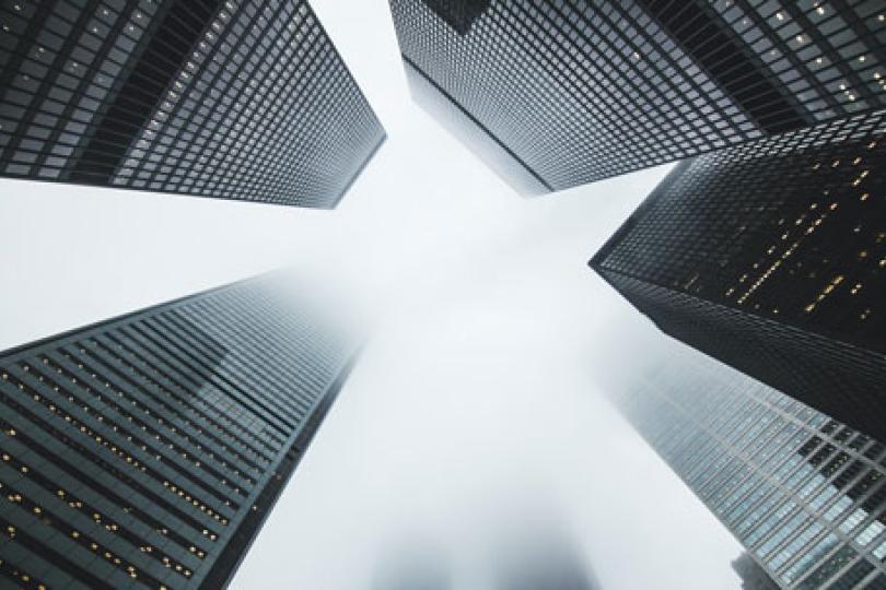 Looking up from the ground at a circle of five skyscrapers disappearing into clouds