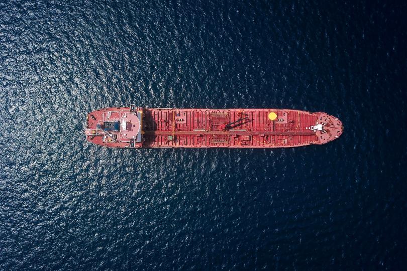 A large red ship is seen from far above, surrounded by dark blue/black water. 